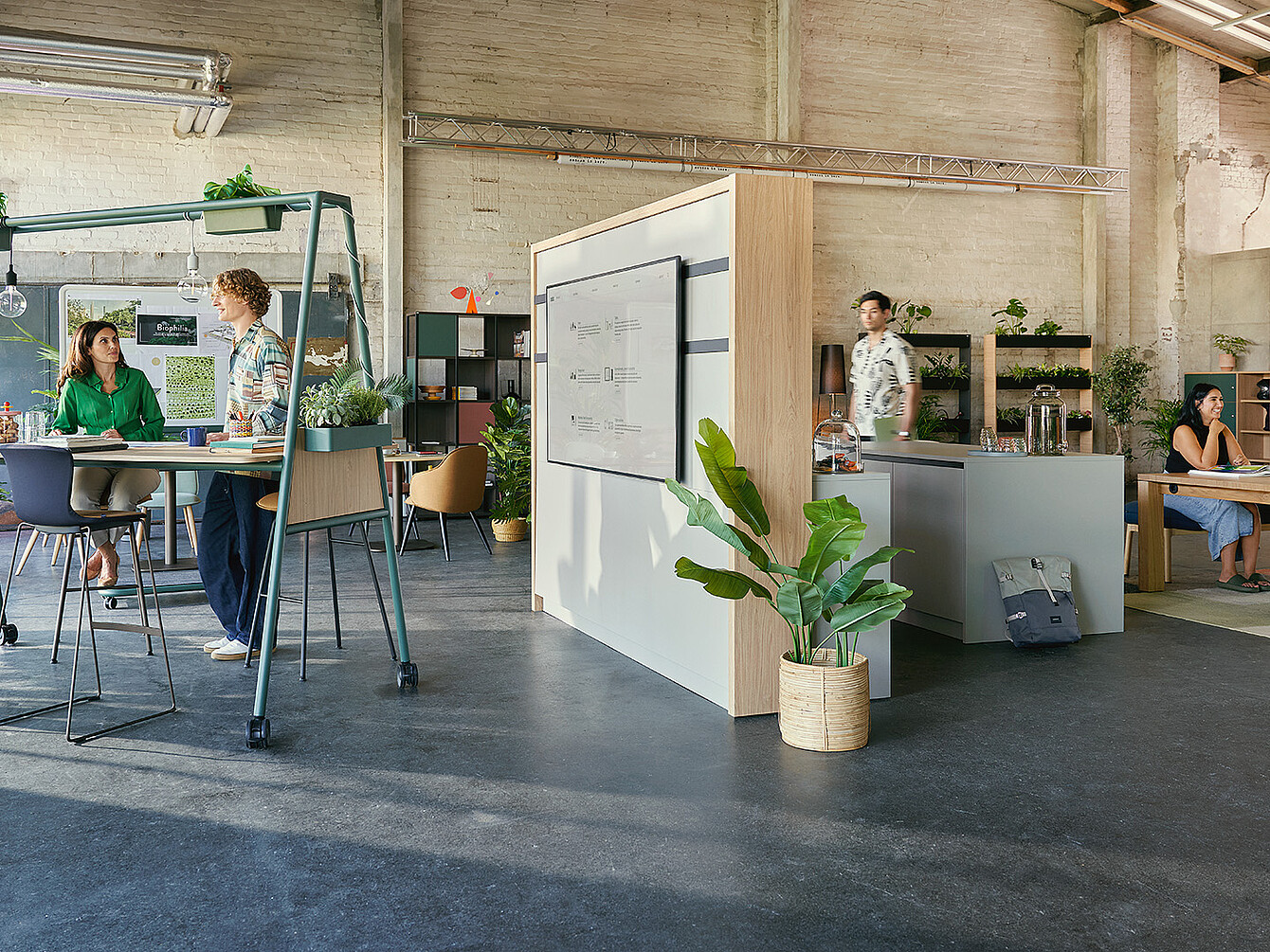 Un moderno Smart Café in un ufficio che unisce lavoro e relax, con persone che interagiscono su tavoli alti e sedute lounge, circondate da piante e luce naturale.