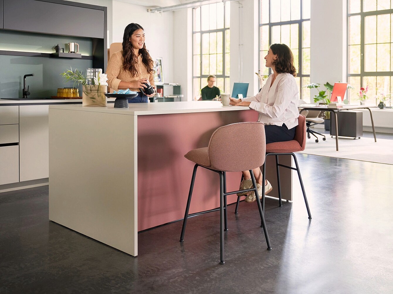 Two women at a café bar one standing behind the counter and the other sitting on a high chair holding a cup