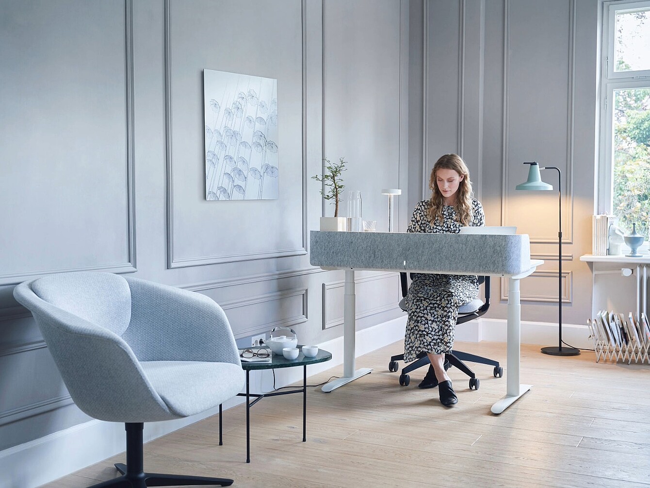 Personne assise à un bureau moderne dans un bureau à domicile lumineux, avec un fauteuil clair, une petite table ronde et une décoration murale