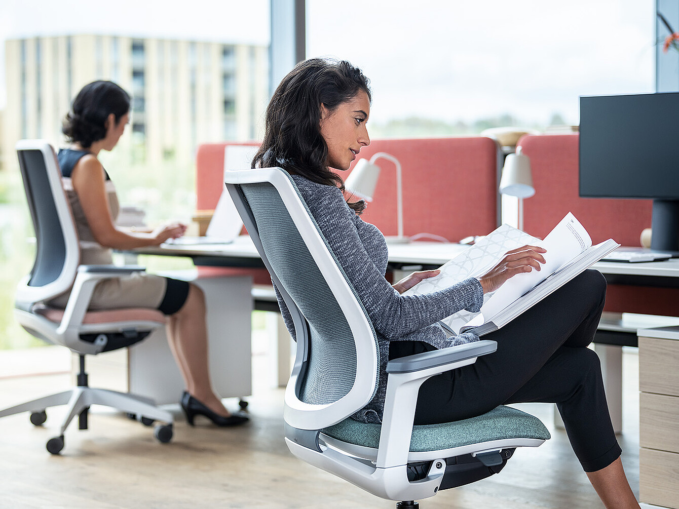 Deux femmes travaillant dans un bureau moderne, l’une lisant des documents et l’autre tapant sur un ordinateur portable