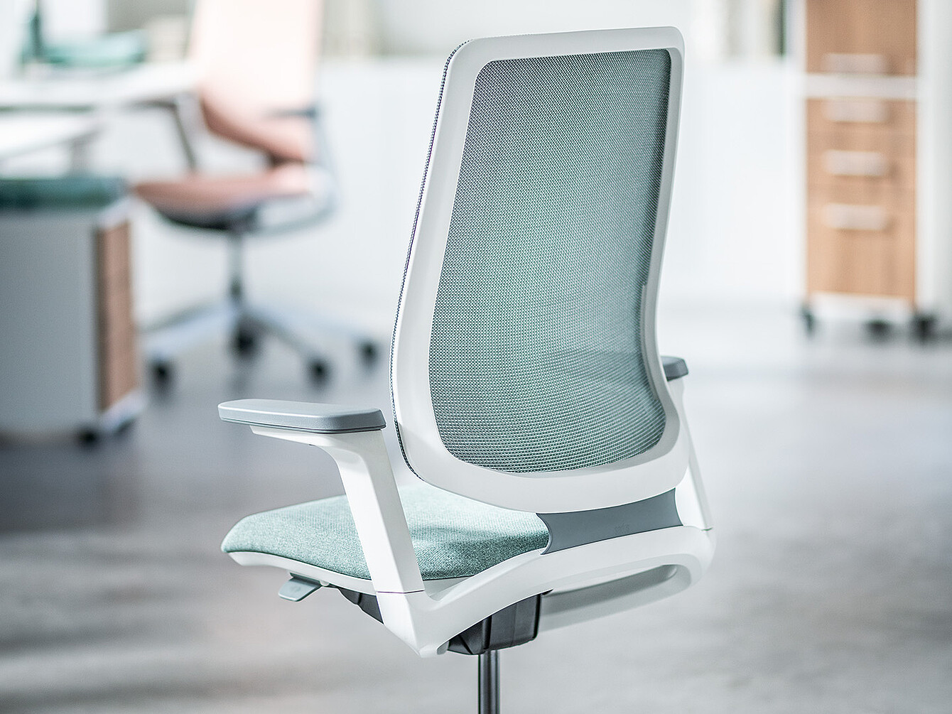 Siège de bureau ergonomique vert clair avec dossier en maille et structure blanche dans un environnement de bureau moderne