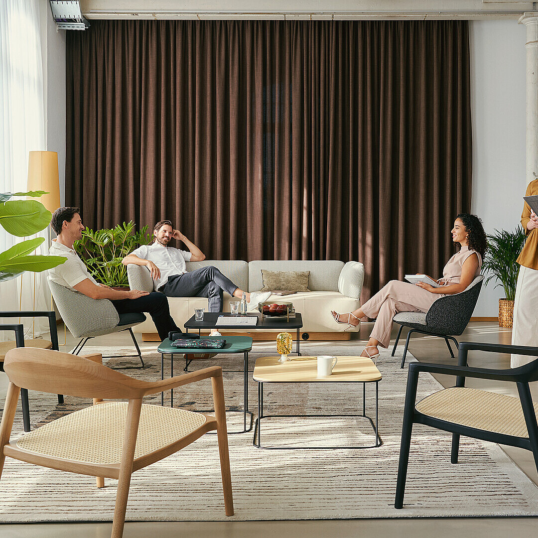 Work Café Club room with modern seating including sofas and chairs around coffee tables, plants, and large windows creating a relaxed, stylish business lounge atmosphere