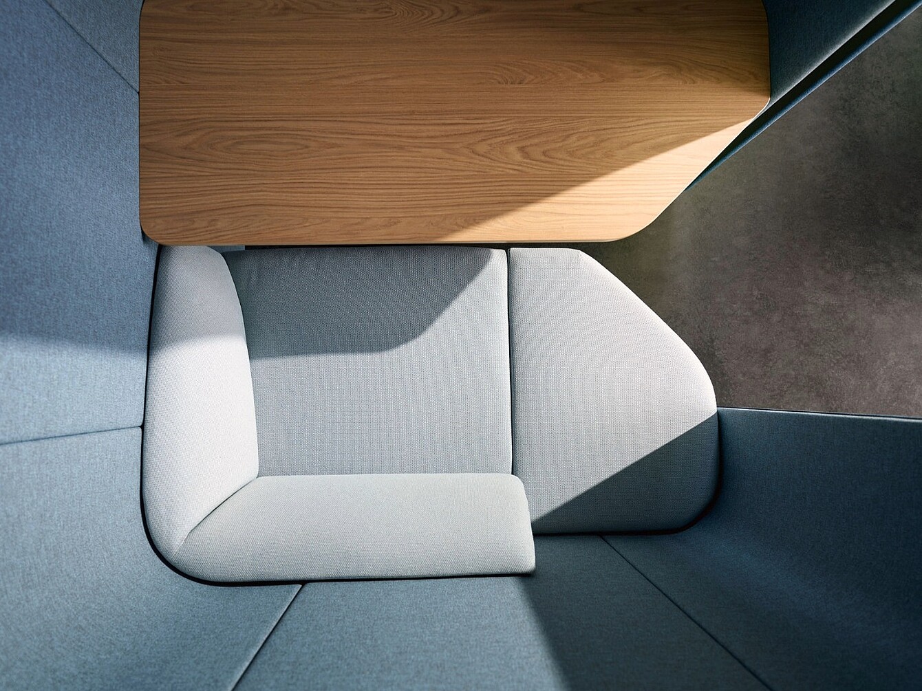 Top-down view of a modular seating unit with light gray cushions and a wooden table surface in a corner space.