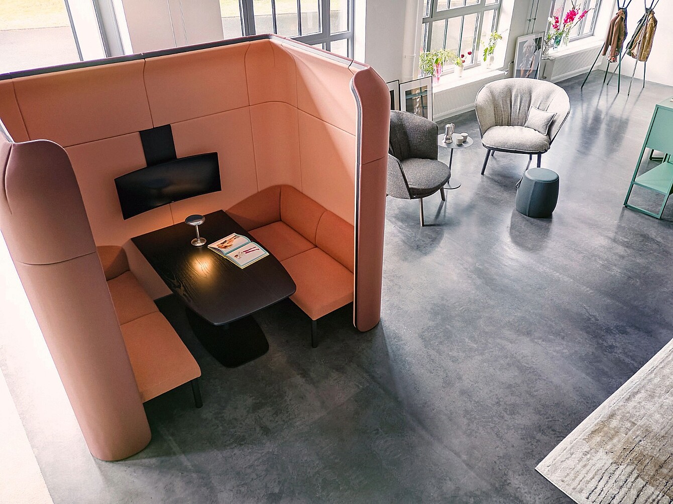Cabina curva con pareti alte, panca integrata e tavolo nero all’interno di una sala aperta con due poltrone e un piccolo tavolo rotondo nelle vicinanze