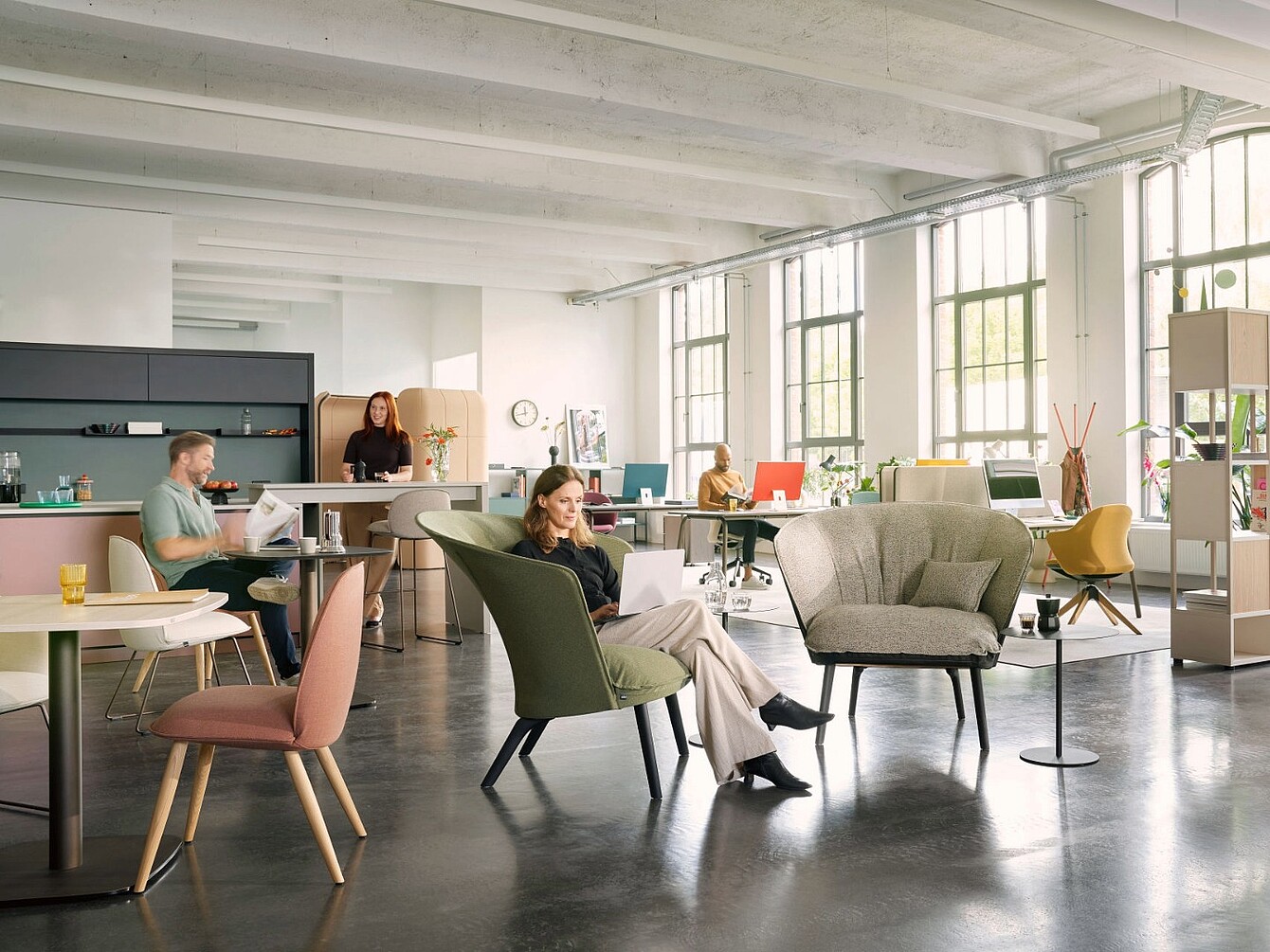 Bureau en open space doté de grandes baies vitrées, où plusieurs personnes travaillent à leur bureau ou sont assises dans des fauteuils, avec un mobilier moderne et un agencement spacieux
