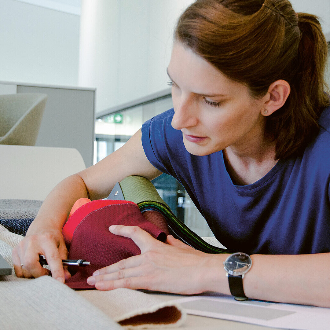 Industrial designer Judith Daur selecting fabrics and materials, focused on a colorful textile swatch, in a modern workspace.