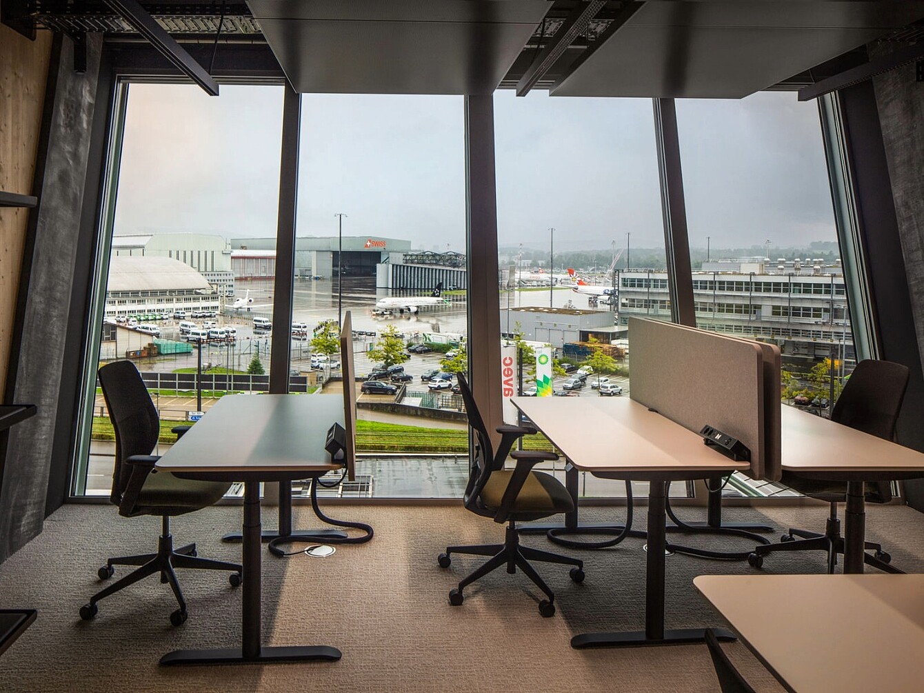 Espace de travail avec des sièges et des bureaux Sedus face à de grandes fenêtres donnant sur l’aéroport de Zurich et les avions stationnés.