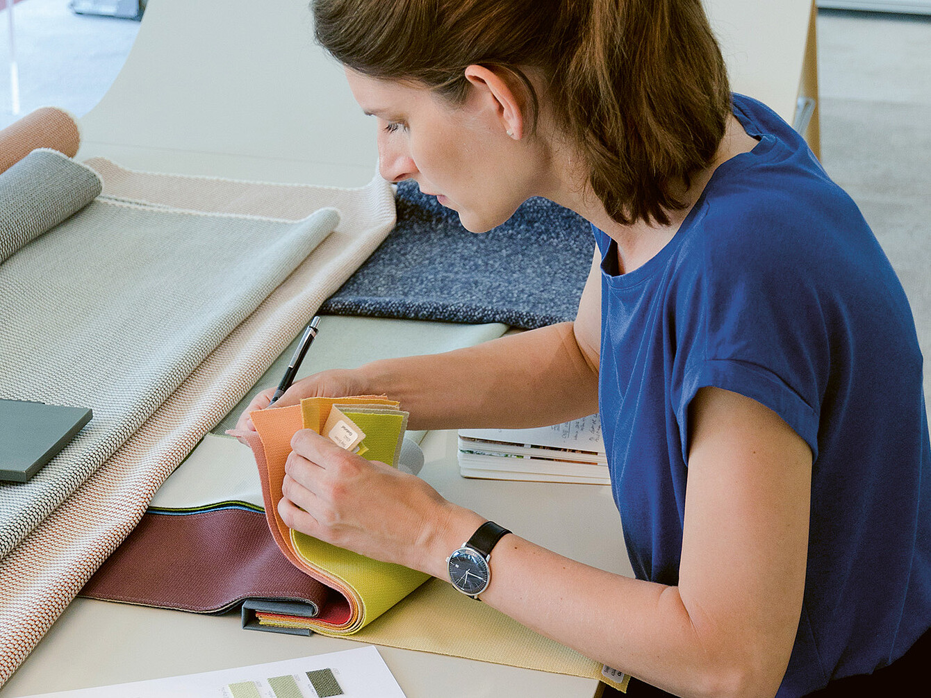 La designer industriale Judith Daur esamina campioni di tessuto, concentrandosi su colore e consistenza, in uno spazio di lavoro pieno di materiali diversi. 