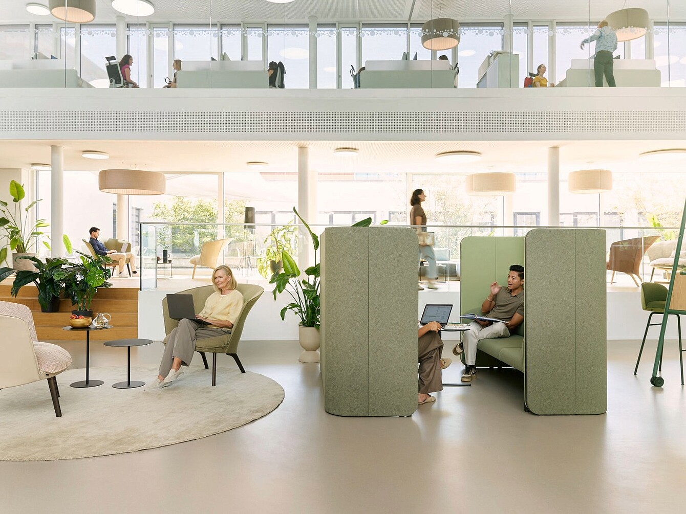 Intérieur de bureau moderne avec des zones de travail ouvertes, des cabines de confidentialité capitonnées vertes, des plantes et de grandes fenêtres laissant entrer la lumière naturelle