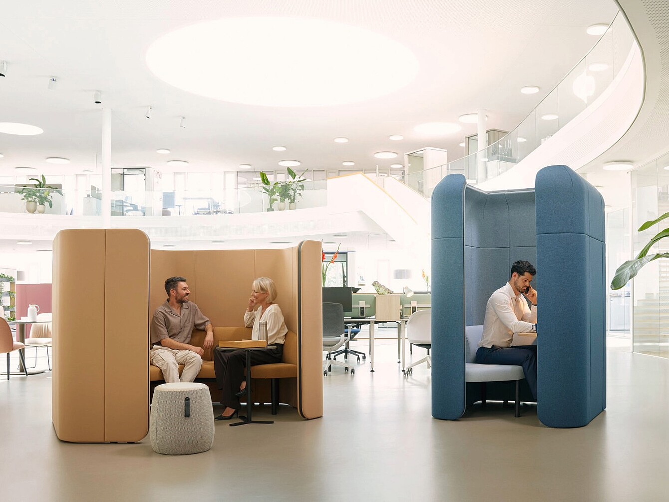 Due persone sedute in unità se:hive separate con pareti imbottite alte in un ufficio open space con scrivanie e piante sullo sfondo