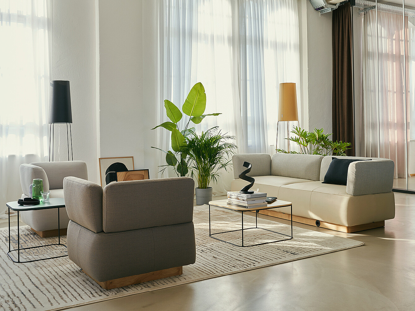 Espace illustrant l’archétype du Work Café Club avec canapés beiges, lampadaires noirs et jaunes, plantes vertes et tables basses minimalistes dans un salon d’affaires lumineux et élégant.