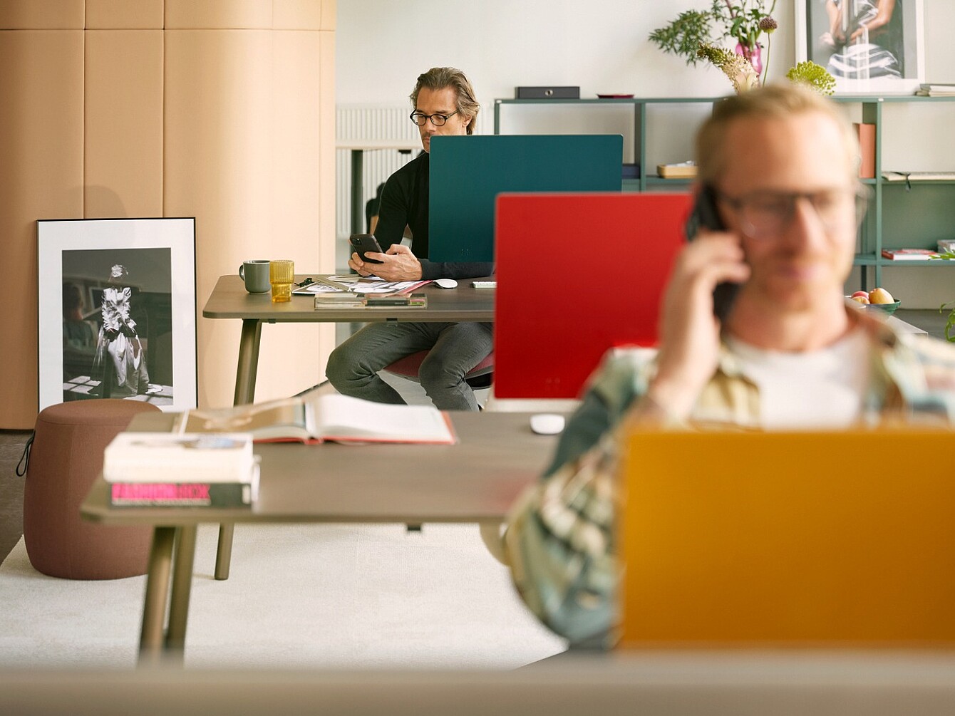 Deux collaborateurs travaillant à leur bureau derrière des écrans de confidentialité colorés, tandis qu’une personne au premier plan passe un appel téléphonique.
