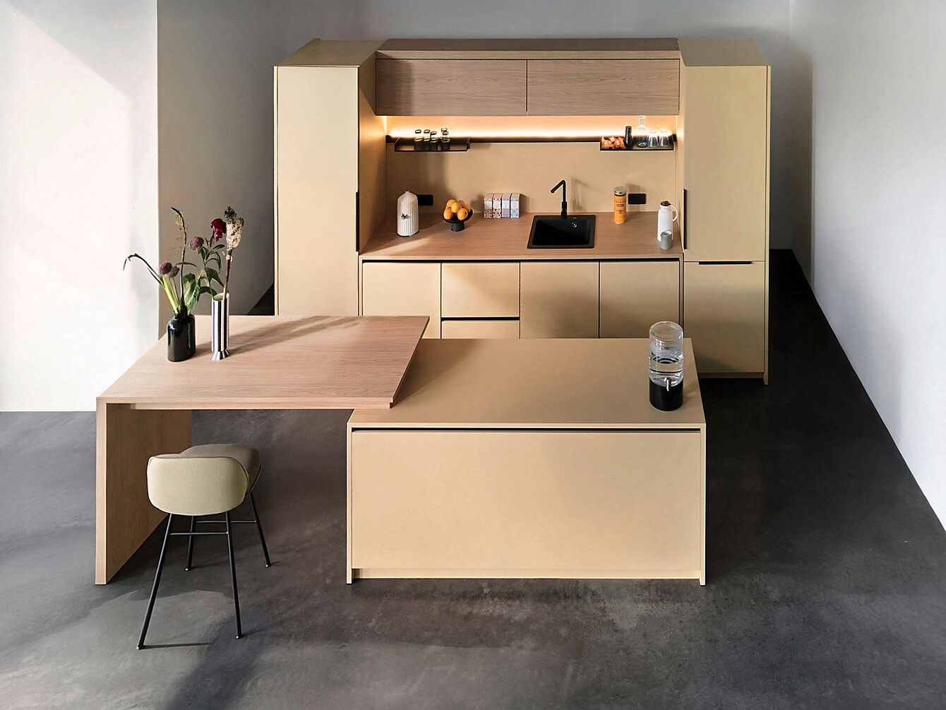 Minimalist se:café bar setup with tall beige cabinets, integrated sink, under-cabinet lighting, wooden countertop extension with a stool, and decorative vases with flowers