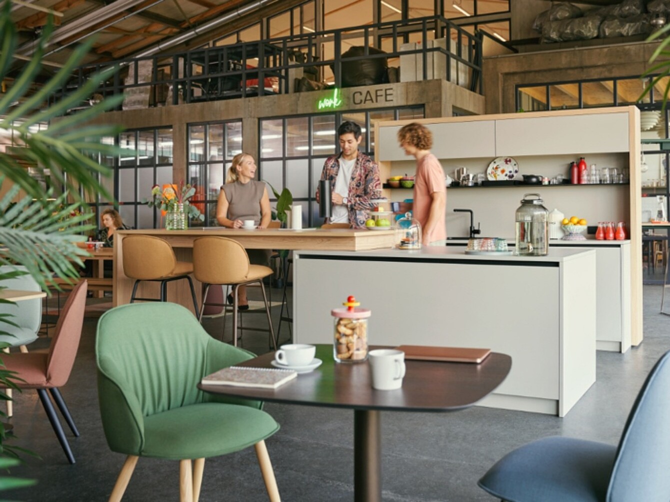 Three people talking at a modern café counter in an open space with seating and plants