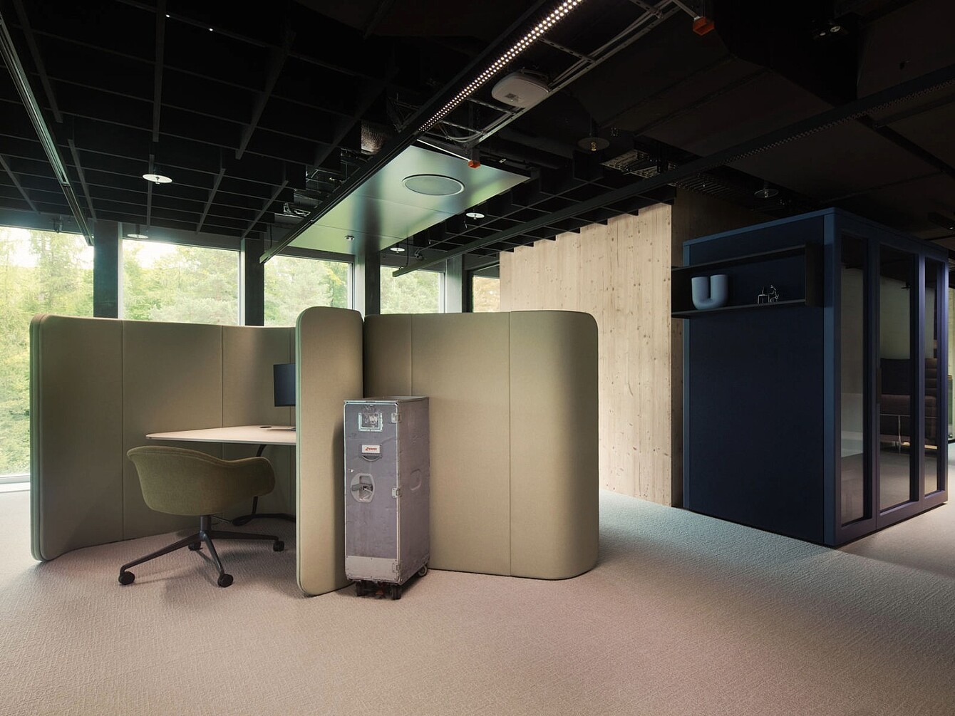 Espace de travail avec une cloison incurvée (se :hive) beige entourant un bureau et une chaise pivotante vert olive, à côté d’un coffre de rangement en métal 