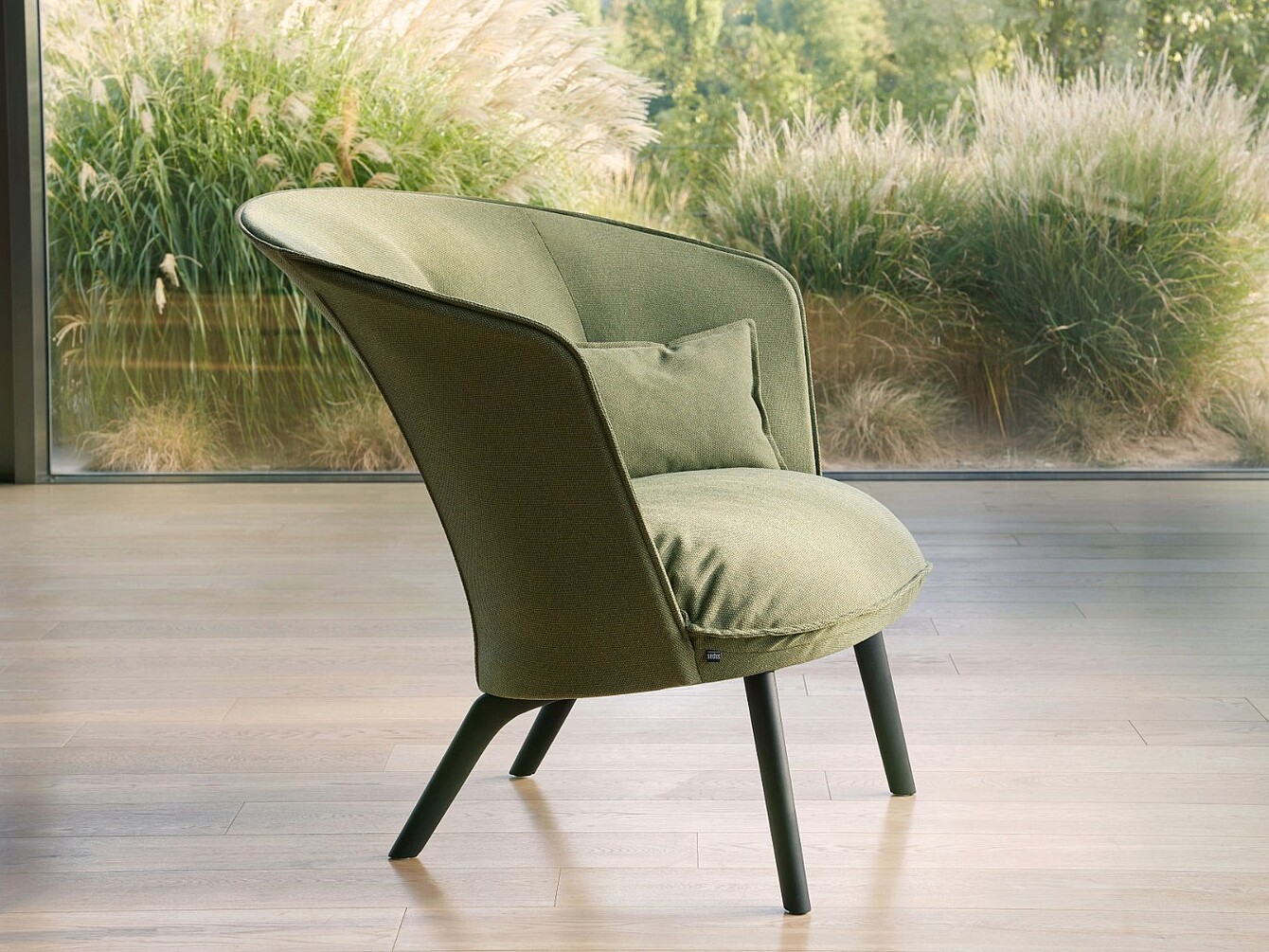 Fauteuil moderne avec revêtement en tissu vert et petit coussin, devant une grande baie vitrée donnant sur des plantes de jardin