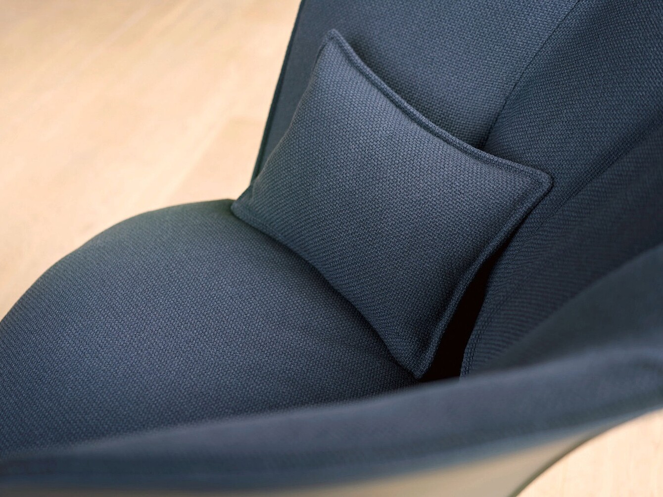Gros plan sur un fauteuil en tissu foncé avec un petit coussin assorti posé sur l’assise