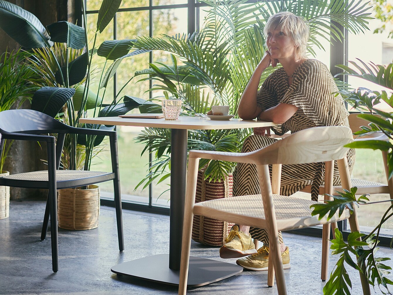 Persona sentada en una mesa en una sala con grandes ventanas y varias plantas de oficina a su alrededor
