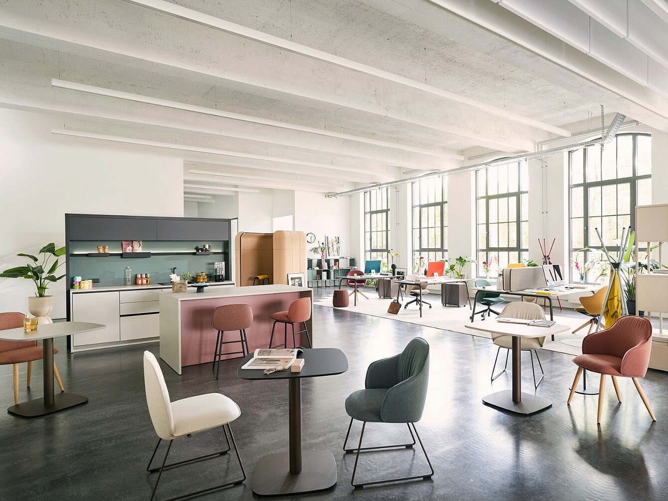 Espace de bureau ouvert avec de grandes fenêtres, divers agencements de sièges, notamment des fauteuils et des tables, un coin cuisine et des plantes