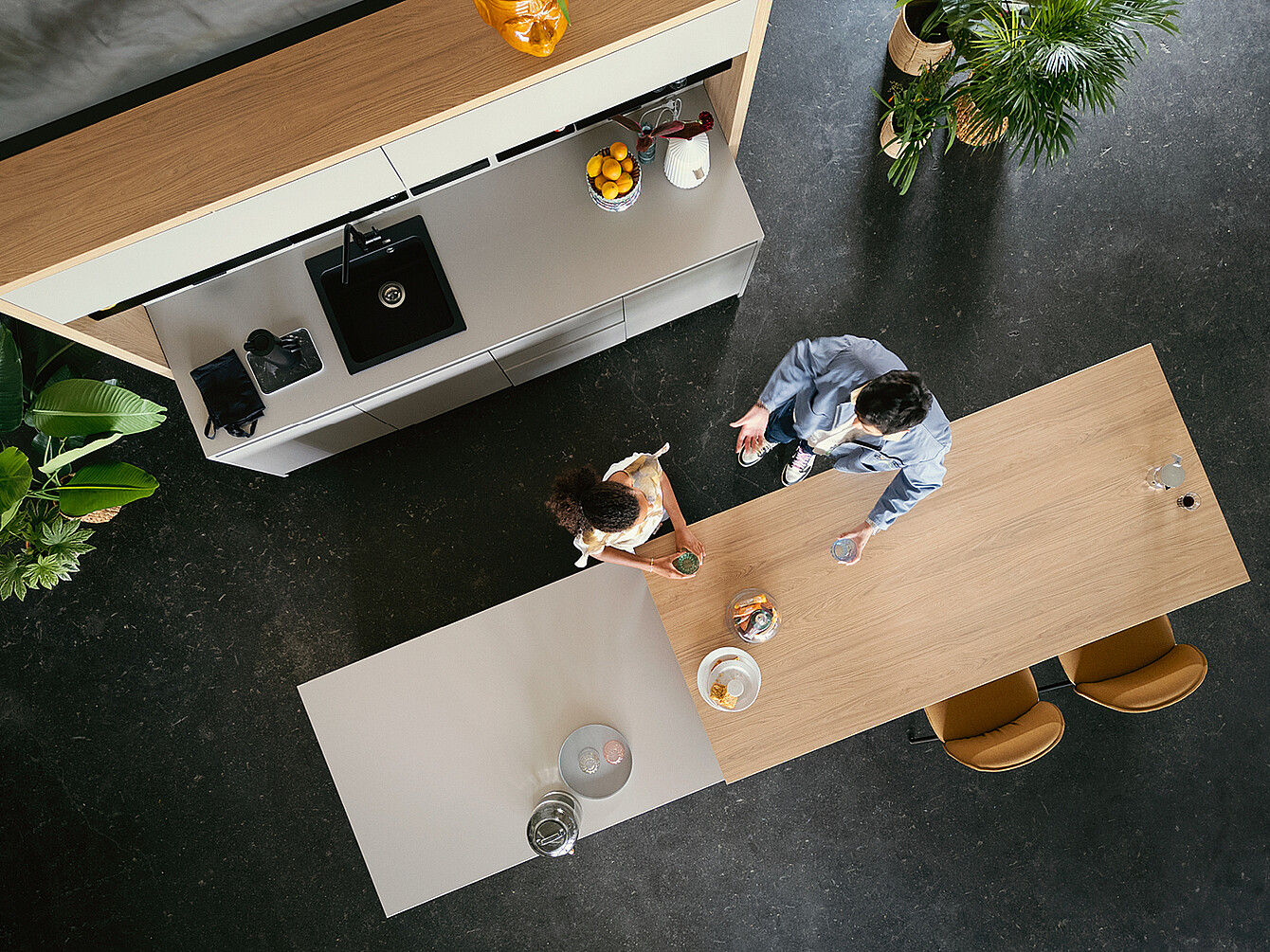Vue aérienne de deux personnes discutant autour d’une table en bois dans un espace de travail hybride moderne et convivial, avec coin cuisine intégré et plantes