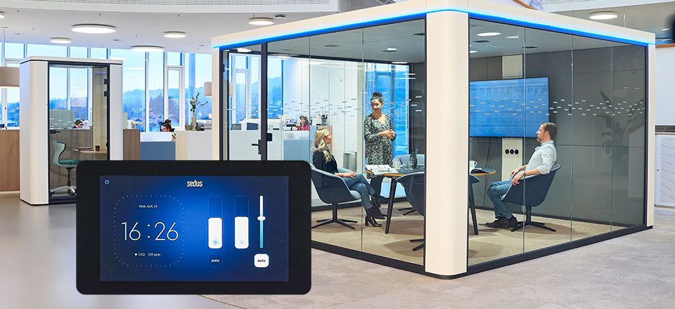 Ufficio moderno con soluzione se:cube room-in-room a pareti di vetro con illuminazione a LED blu e persone all’interno, con un primo piano del nuovo display touch che controlla illuminazione e ventilazione